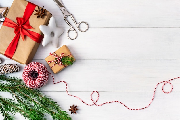 Préparation pour les vacances, emballage de cadeaux, vue de dessus avec espace de copie. Fond avec des coffrets cadeaux en papier craft, corde à rayures, biscuits festifs et une branche d'un arbre de Noël sur une table en bois blanche.