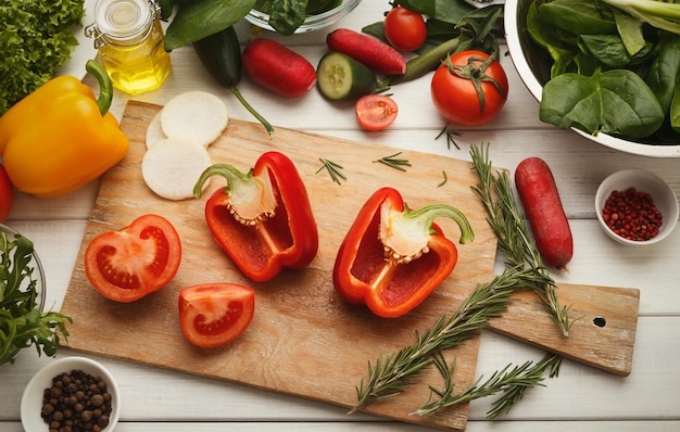 Préparation d'une salade de légumes frais à la vue de dessus de table de cuisine. Couper le poivron rouge mûr et la tomate sur planche de bois, espace de copie