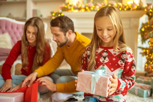 Préparations agréables. Jeune famille emballant des cadeaux de Noël et à la recherche de participation