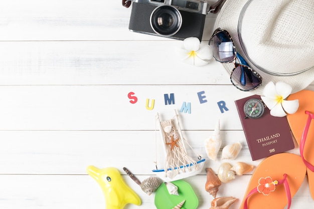 préparer des accessoires et des articles de voyage pour l'été, chapeau, lunettes de soleil et pantoufles de plage sur bois blanc