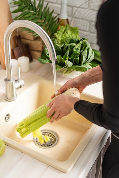 Préparer des aliments sains. Jeune femme souriante en vêtements de sport, laver le céleri dans la cuisine