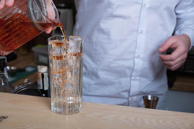 Préparer un cocktail alcoolisé avec de la glace dans un verre au bar