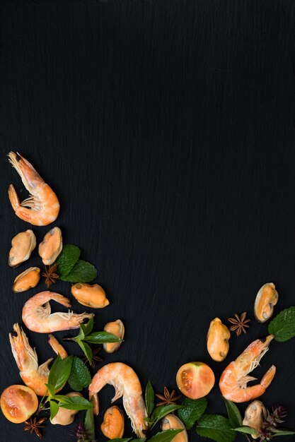 Photo préparer des fruits de mer frais dans la cuisine avec des crevettes roses et des moules gastronomiques entourées d'herbes fraîches et d'épices sur fond de pierre noire