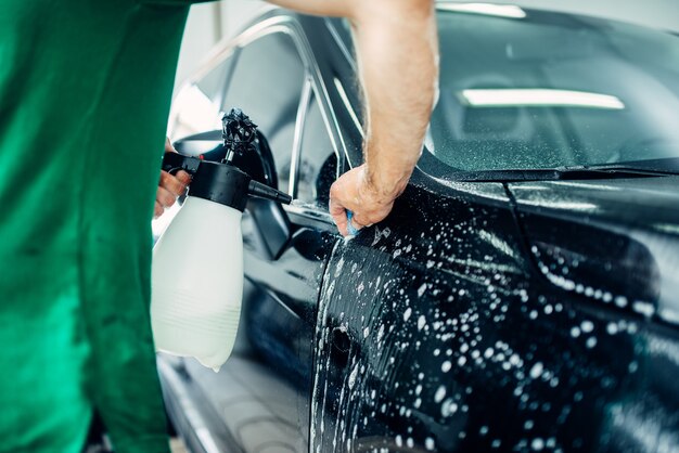 Préparer la voiture, protéger contre les éclats et les rayures. Le travailleur disperse de l'eau savonneuse.