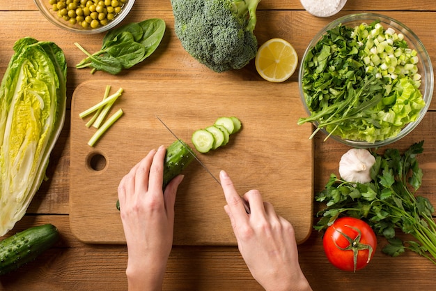 Préparez une salade de légumes frais. Couper le concombre frais sur une planche à découper. Mains féminines.