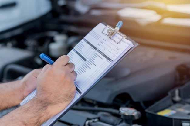 Photo un préposé à l'entretien automobile vérifie une liste du moteur de la voiture pour un client de l'atelier.