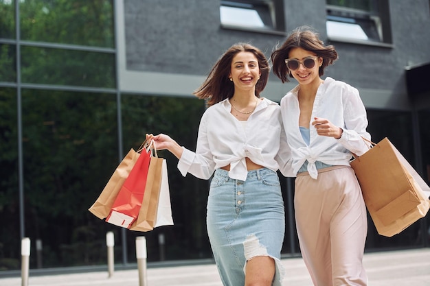 Près d'un bâtiment moderne Deux amies ont une journée de shopping Marcher à l'extérieur avec des sacs
