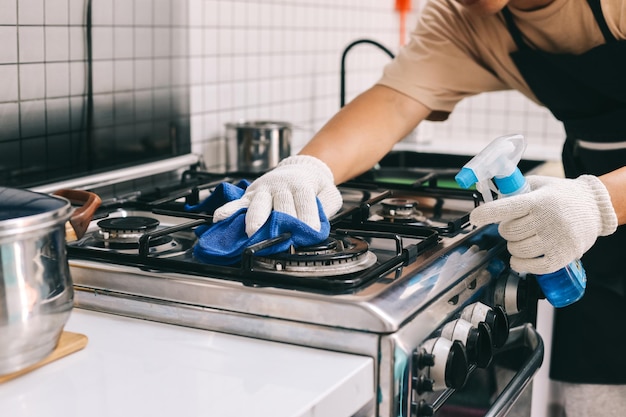 Près des mains nettoyant le poêle de cuisine avec une bouteille de détergent et un chiffon