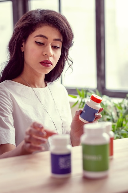 Prescription des médecins. Belle femme intelligente regardant son médicament tout en choisissant lequel prendre