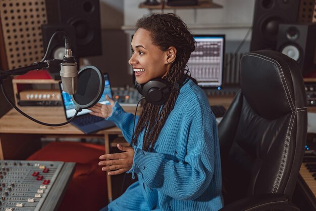 Un présentateur de radio multiethnique agréable enregistre un podcast à l'aide d'un casque et parle dans un microphone dans un studio d'enregistrement