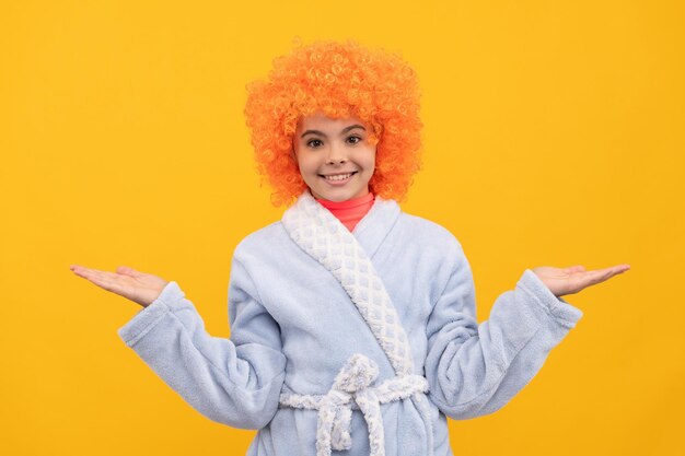 Présentation du produit sur l'espace de copie choix bonheur de l'enfance anniversaire ou soirée pyjama drôle enfant en perruque de clown bouclé enfant fantaisie dans la maison peignoir heureux adolescente aux cheveux orange en vêtements de nuit confortables