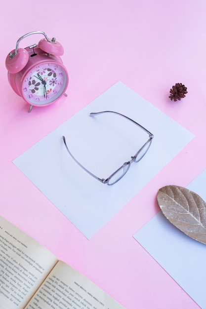 Présentation du produit de Minimalist Concept Idea lunettes livre horloge feuilles sèches sur fond de papier rose