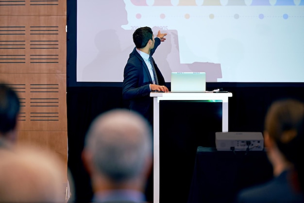 Présentation d'homme d'affaires et point à l'écran de projecteur conférence ou atelier avec ordinateur portable pour diaporama ou PPT Séminaire de formation d'entreprise et conférencier avec public d'information et discours professionnel