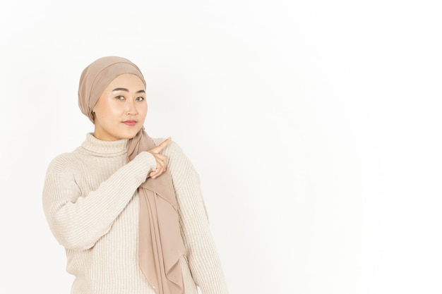 Présentation et pointage de côté de la belle femme asiatique portant le hijab isolé sur fond blanc
