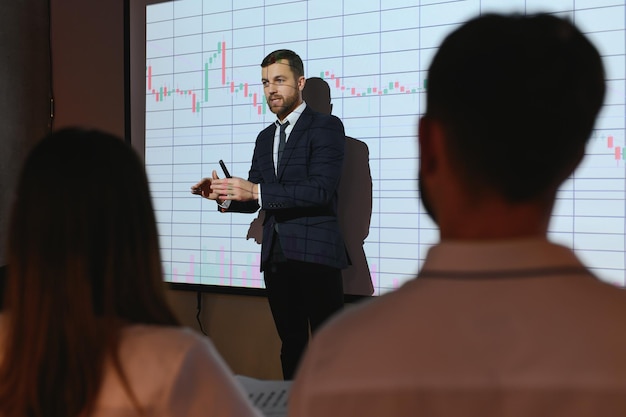 Présentation de la réunion de conférence d'affaires L'homme d'affaires fait l'analyse financière parle à un groupe d'hommes d'affaires L'écran du projecteur montre les données boursières Stratégie d'investissement Croissance des revenus