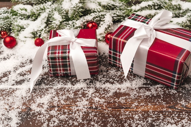 Présente sur fond de bois avec des branches de sapin et des boules rouges saupoudrées de neige