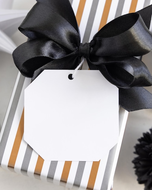 Présenter avec une étiquette-cadeau vierge et un arc noir en gros plan Boîtes-cadeaux enveloppées dans du papier géométrique à rayures et chevrons près d'un décor noir et blanc Maquette d'étiquette d'anniversaire de Noël Nouvel An Anniversaire