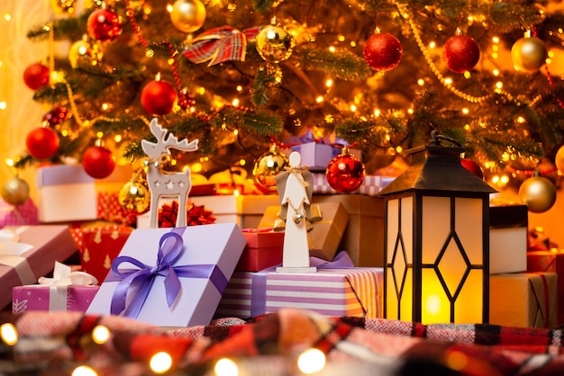 Présentez des boîtes de petites bagatelles sucrées et une lanterne sous un arbre de noël décoré brillant