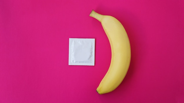 Préservatif et banane sur fond rose. Notion de sexe