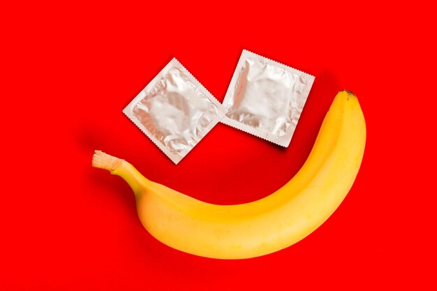 Un préservatif et une banane, sexe sans risque. Jouet sexuel. Sur fond rouge.