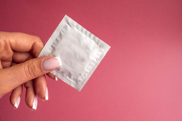 Le préservatif prêt dans la main d'une femme donne le concept de rapports sexuels protégés un préservatif sur le lit Prévenir l'infection et les contraceptifs contrôler la fertilité ou des mesures préventives sûres Journée mondiale du sida Laisser de l'espace pour le texte