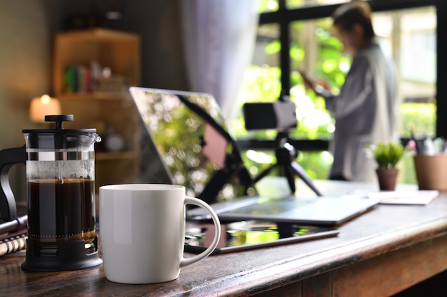 Une presse à café et une tasse sur un bureau avec une personne travaillant à domicile