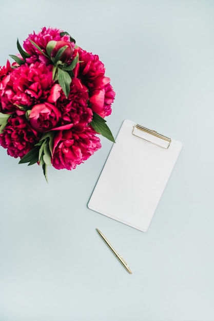 Presse-papiers et bouquet de fleurs de pivoines roses sur une surface bleu pastel