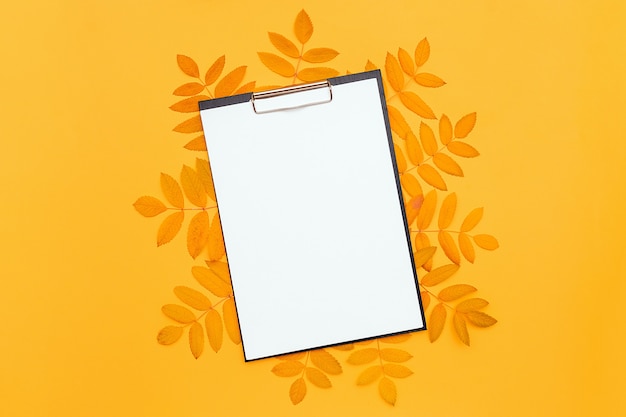 Presse-papiers avec du papier blanc blanc et des feuilles d'automne sur fond jaune