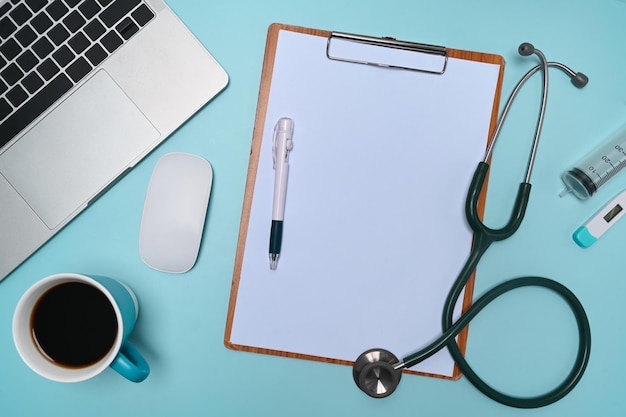 Presse-papiers, ordinateur portable, stéthoscope et tasse à café sur l'espace de travail du médecin.