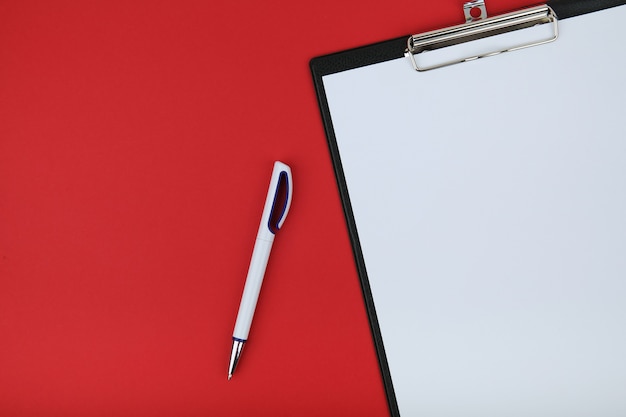 Presse-papiers avec papier vide et stylo sur fond rouge