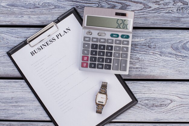 Presse-papiers avec plan d'affaires avec calculatrice et horloge de montre. Vue de dessus à plat. Table en bois blanc.