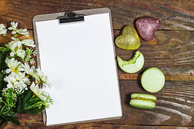 Presse-papiers vide avec des fleurs de marguerite et des macarons et des paillettes de coeur sur une table en bois