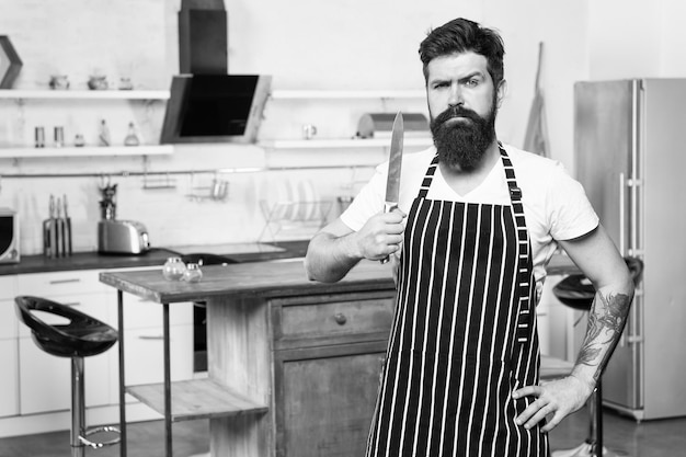 Prêt à couper le chef sérieux et confiant dans le café utiliser un couteau cuisine savoureuse homme barbu hipster dans la cuisine homme brutal dans le tablier de cuisinier homme mûr avec barbe cuisine affaires culinaires processus de cuisson