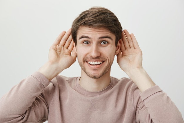 Prêt à écouter les derniers potins. Portrait d'un bel homme européen excité tenant des paumes près des oreilles et souriant avec une expression ravie