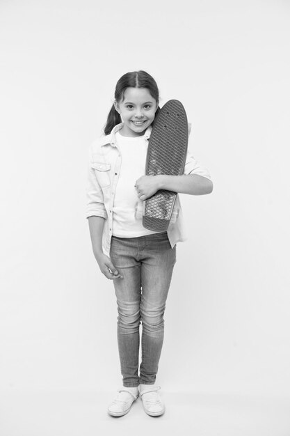 Prêt à monter Kid girl happy porte penny board L'enfant aime faire du skateboard avec penny board Passe-temps adolescent moderne Comment faire du skateboard Fille visage heureux porte penny board fond jaune