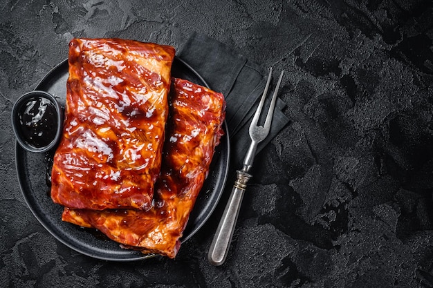 Prêt pour les côtes levées de porc crues au barbecue avec sauce barbecue Fond noir Vue de dessus Espace de copie