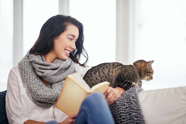 Prêt pour une histoire chat minou Photo d'une jeune femme lisant un livre avec son chat à côté d'elle