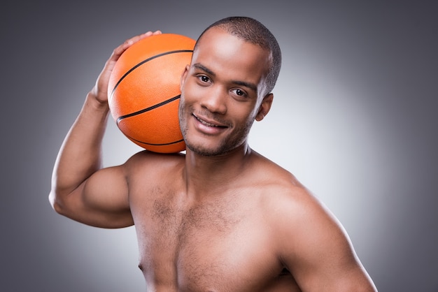 Prêt pour un match. Jeune homme africain torse nu tenant un ballon de basket-ball et regardant la caméra