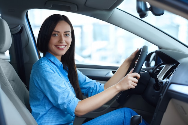 Prêt pour la route. Belle jeune femme souriante joyeusement à la caméra tout en étant assis dans une nouvelle voiture au salon de l'automobile