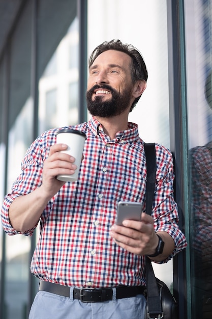 Prêt pour le travail. Agréable bel homme souriant tout en se tenant près de l'immeuble de bureaux