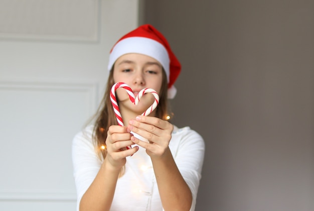 Preteen fille mignonne dans le chapeau de père Noël rouge faisant le coeur de deux canne en bonbon de Noël rayée