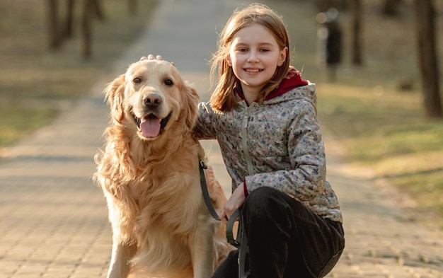 Preteen girl avec chien golden retriever assis à l'extérieur et souriant au printemps