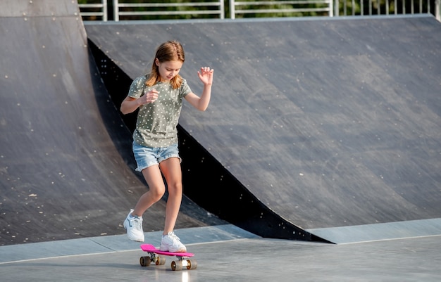 Preteen girl riding sur skateboard à la rampe du parc de la ville. Belle enfant de sexe féminin avec planche à l'extérieur en été