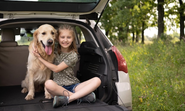 Preteen girl sitting with golden retriever dog dans le coffre de la voiture et souriant en regardant la caméra. Enfant enfant étreignant un animal de compagnie de race pure dans le véhicule à la nature