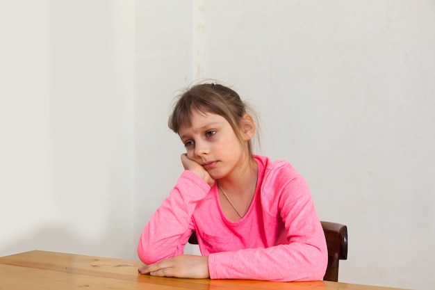 Preteen girl triste en pull rose à table avec une expression triste sur son visage