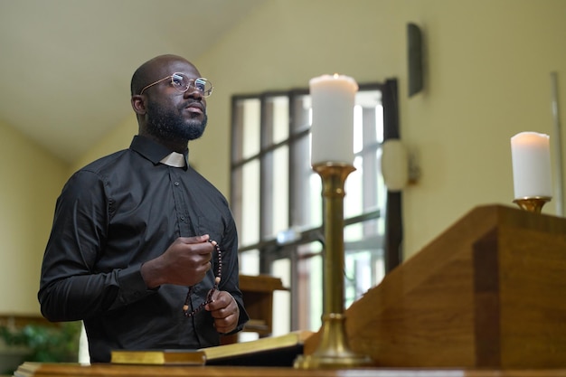 Prêtre afro-américain en tenue décontractée noire tenant un chapelet pendant la prière