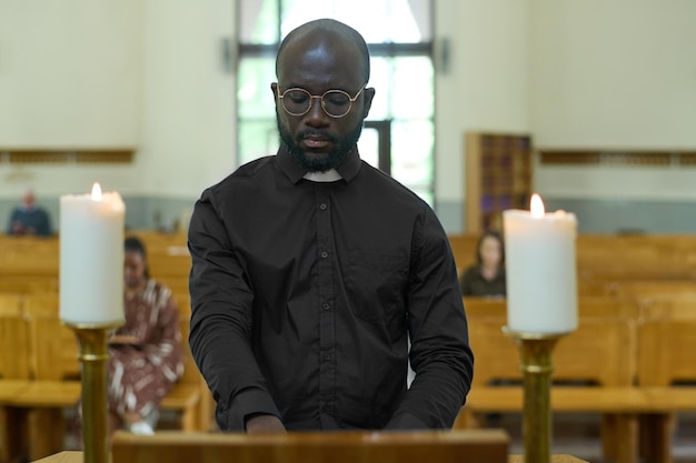 Prêtre debout en chaire entre deux bougies allumées pendant le service religieux