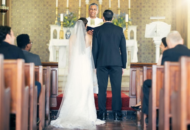 Prêtre de mariage et couple à l'autel pour les vœux de mariage lors d'une cérémonie d'engagement dans une église par derrière Amour marié et mariés attentionnés célébrant leur relation amoureuse dans une chapelle