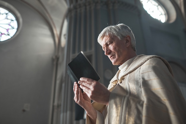 Prêtre principal en costume formel lisant des prières tout en tenant une cérémonie dans l'église