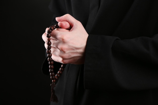Prêtre tenant le chapelet sur fond noir